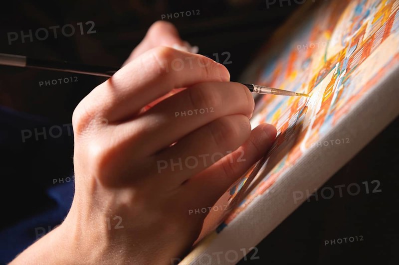 Close-up of a female artist's hand painting with watercolors color on canvas with a brush in a dark modern art studio. The concept of a young artist or female artist