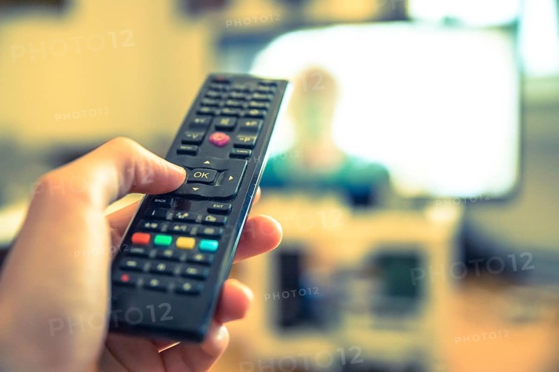 TV remote control in the foreground, tv in the blurry background