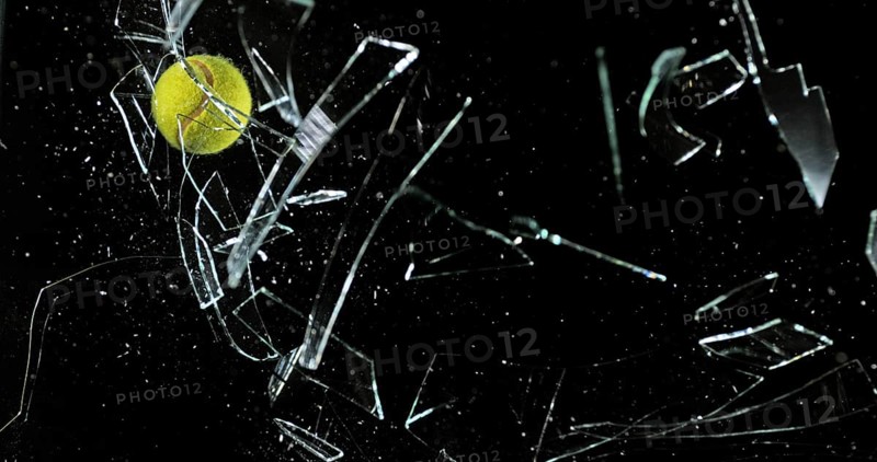 Tennis Ball breaking Pane of Glass against Black Background