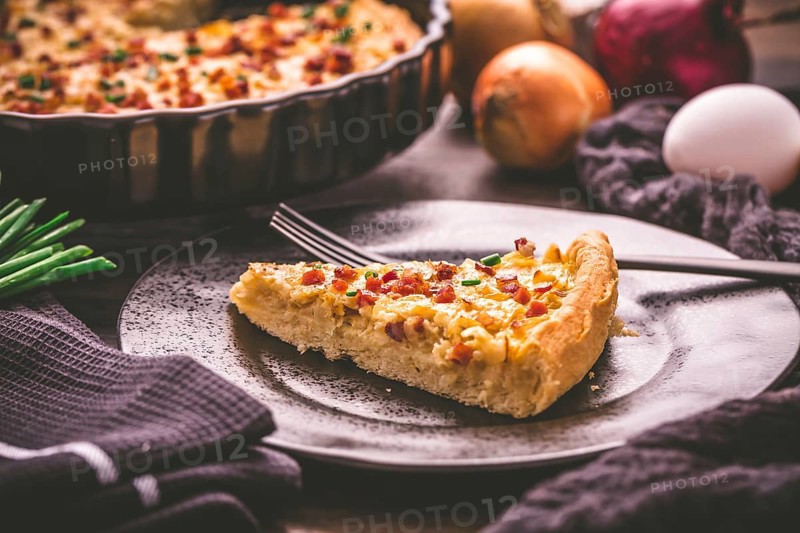 Piece of homemade onion tart or pie with bacon and chive on wooden background