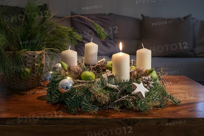 First Advent, wreath with one burning white candle and Christmas decoration on a wooden table in front of the couch, festive home decor, copy space, selected focus, narrow depth of field