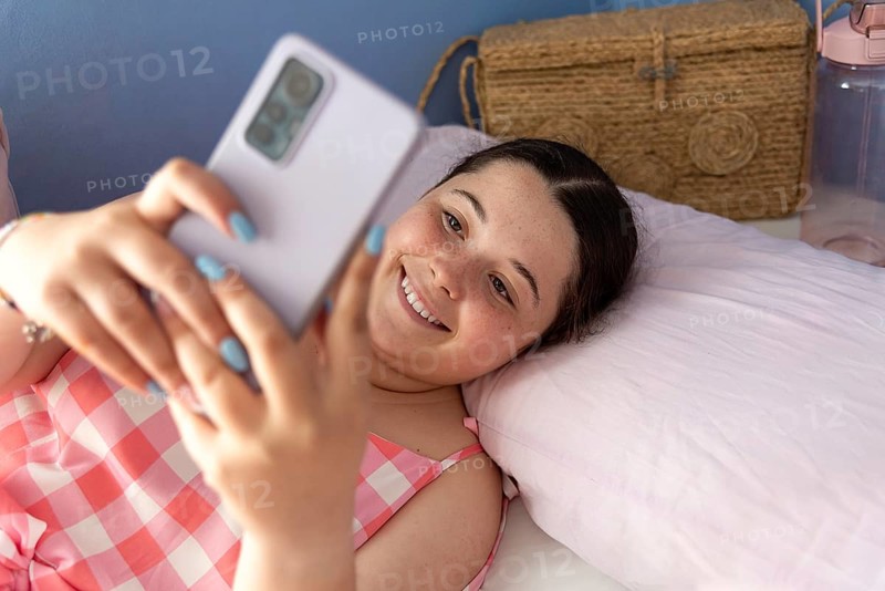 Beautiful and cheerful young Latin American woman in pajamas, taking a selfie with her mobile phone. Expression of happiness and cozy atmosphere, tarragona, spain