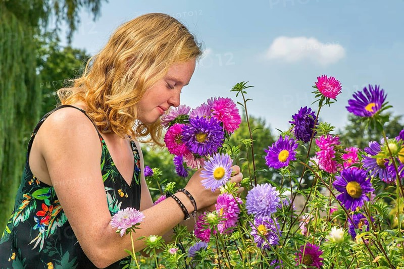 Young dutch redhead woman smelling summer flowers in garden