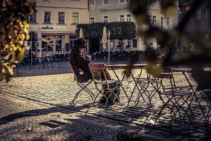 A person sits alone at a café table, reading relaxed in the autumnal atmosphere, On the streets in Weimar