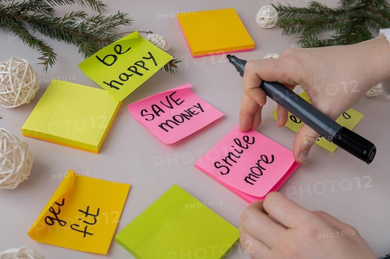 Unrecognizable woman writing new year's resolutions on colorful sticky notes. Making promises for new year, setting goals. Creating vision board motivation