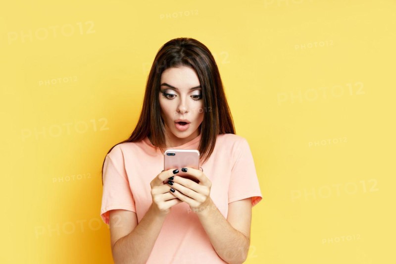 Portrait of a shocked pretty millennial hipster girl using mobile phone isolated over yellow background