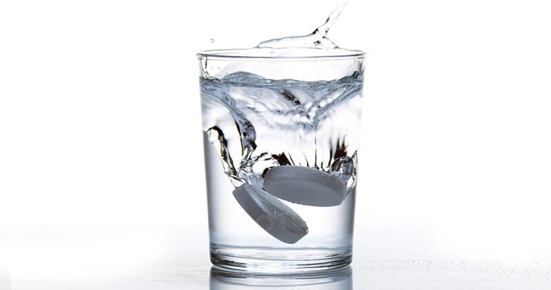 Tablets Falling and Dissolving into a Glass of Water against White Background