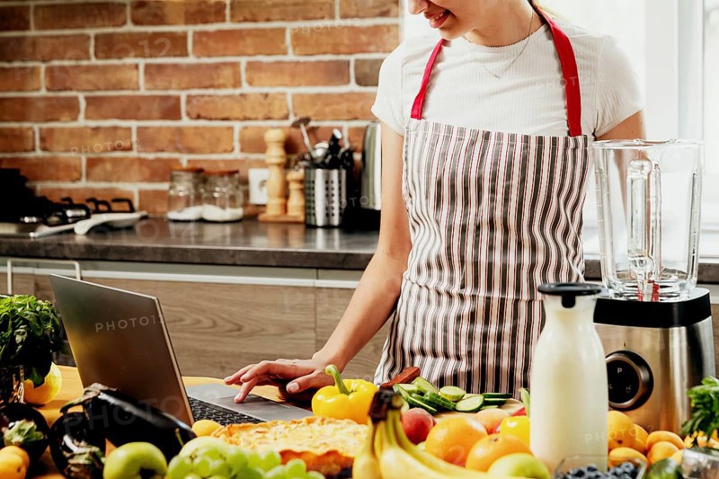 Woman using laptop at home kitchen. Girl touching touchpad with hand, searching for a recipe. Chef using pc, online food shopping on computer. Delivery app ads concept, cook book or diet plan recipes