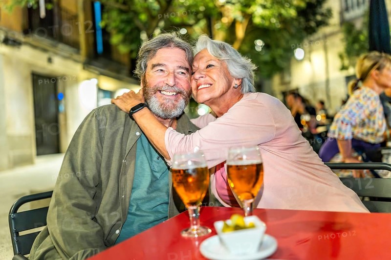 Senior happy couple embracing drinking beer in sidewalk bar in the city