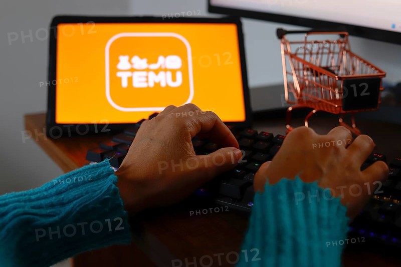 In this photo illustration, a person typing and in the background the Temu logo is displayed on the screen of a tablet