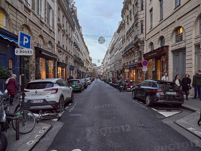 A busy city street at dusk with parked cars and pedestrians, Rue de L'Odeon .Paris