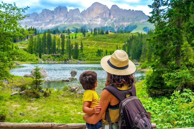 Mother carrying her son while enjoying breathtaking views of emerald waters at lake carezza, surrounded by the dolomites