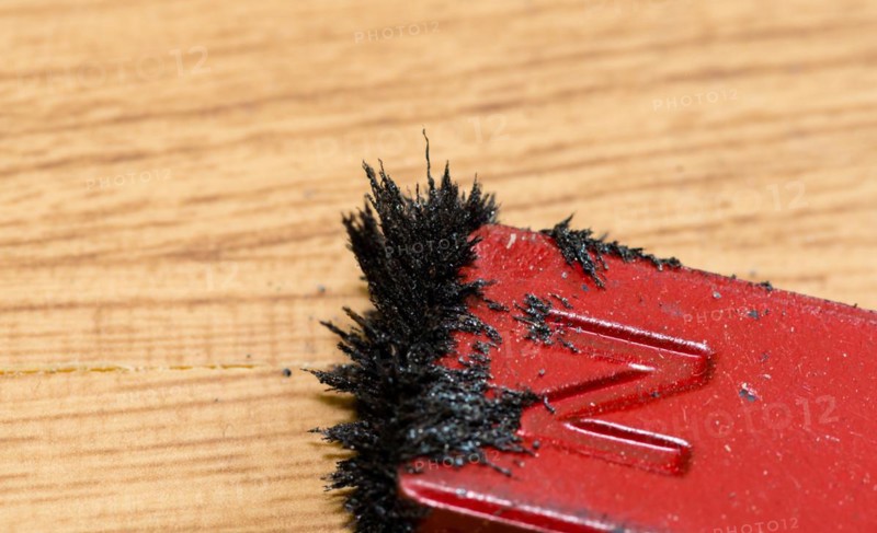 Closeup of iron filings attached to red colored north end of magnet on wood grain background