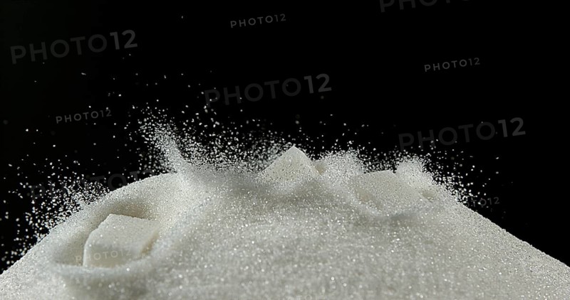White Sugar Cube falling on Powder Sugar against Black Background