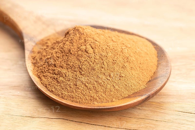 Cinnamon powder in wooden spoon on wooden table. Close up
