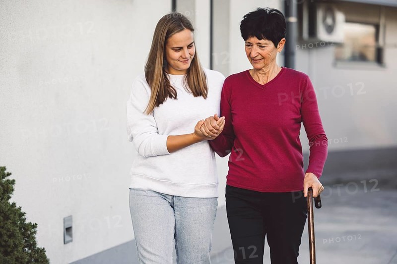 Young caucasian woman a nurse, on a home visit taking care of a senior lady. Nurse helping a senior women with every day chores, helping her to walk and move around the house