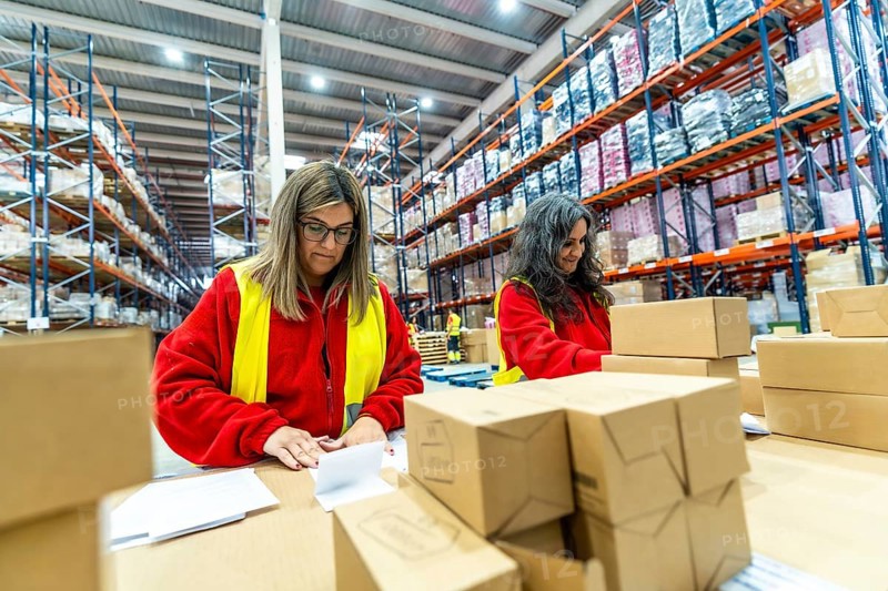 Two female manual workers organizing shipments in a warehouse
