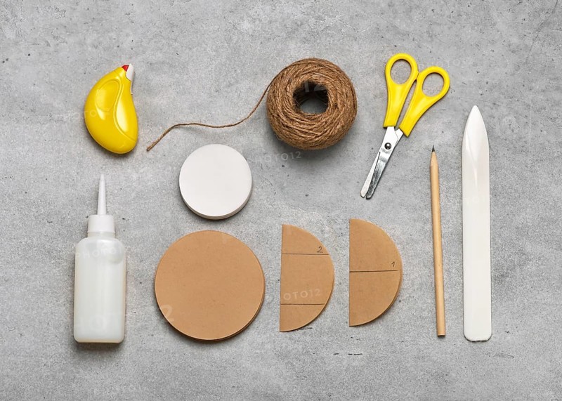 Workplace with craft equipment: brown and white coffee filters, glue, scissors, pencil, jute twine, paper folder for making honeycomb balls. Simple, handmade Christmas decorations with children