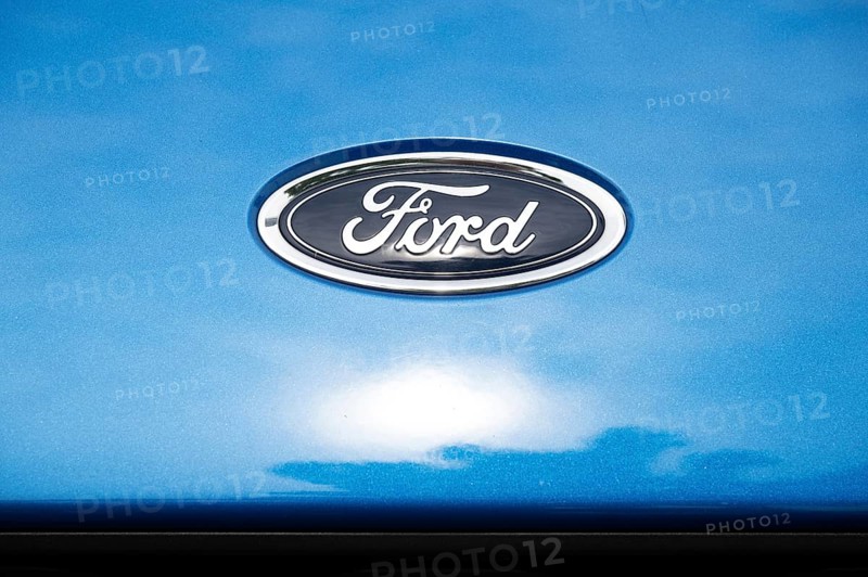 Logo of the car manufacturer Ford, sun behind clouds reflected in the paintwork