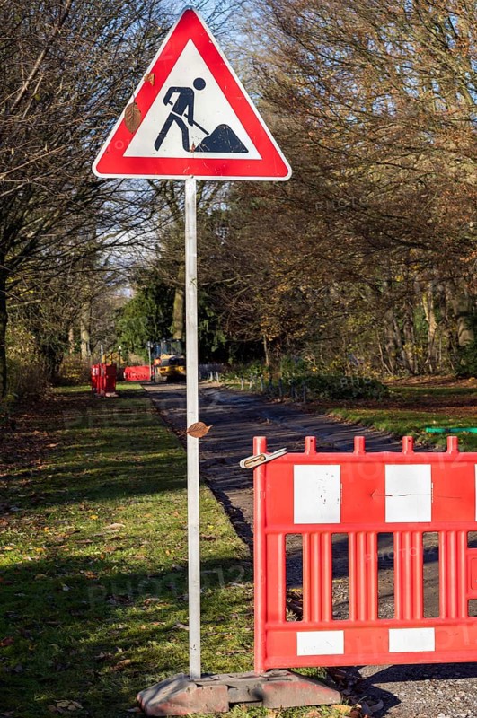 Red and white roadblock and roadworks sign closing a park path for construction