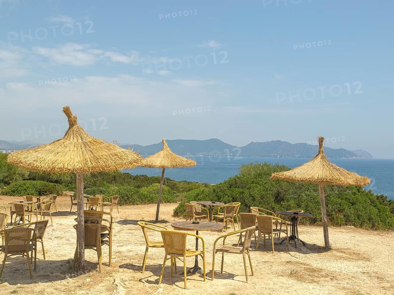 Beach huts with straw parasols, tables and chairs, sea view and mountains in the background in sunny weather, sa coma, mallorca, spain