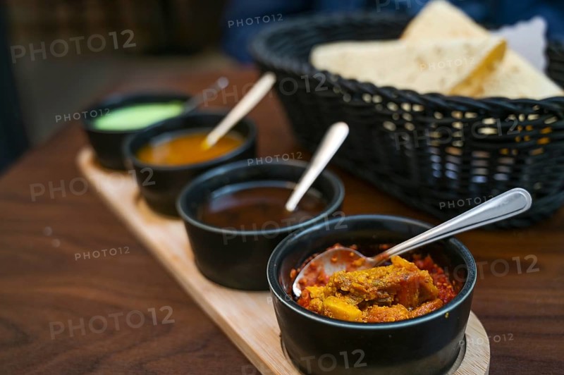 Indian dip, relish, chutney and sauce served in small black bowls with crispy papadam bread on a dark wooden table, copy space, selected focus, very narrow depth of field