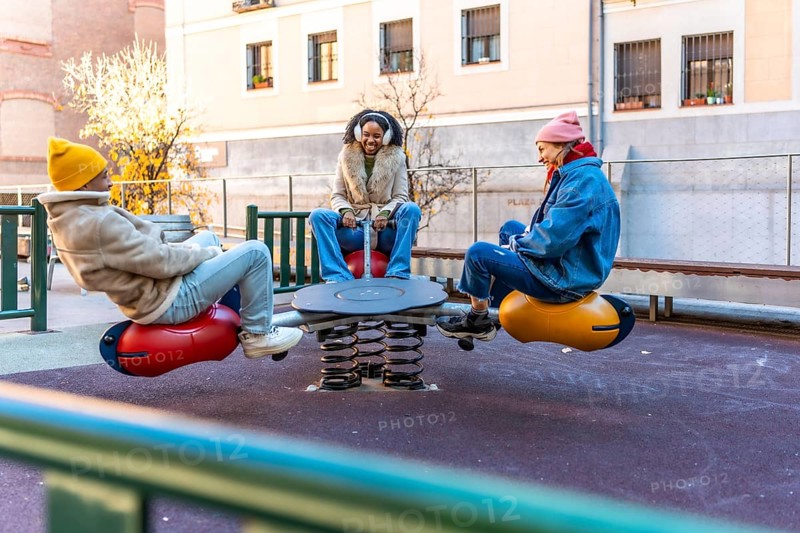 Three friends enjoying a sunny winter day, playing together on a playground seesaw in a city park