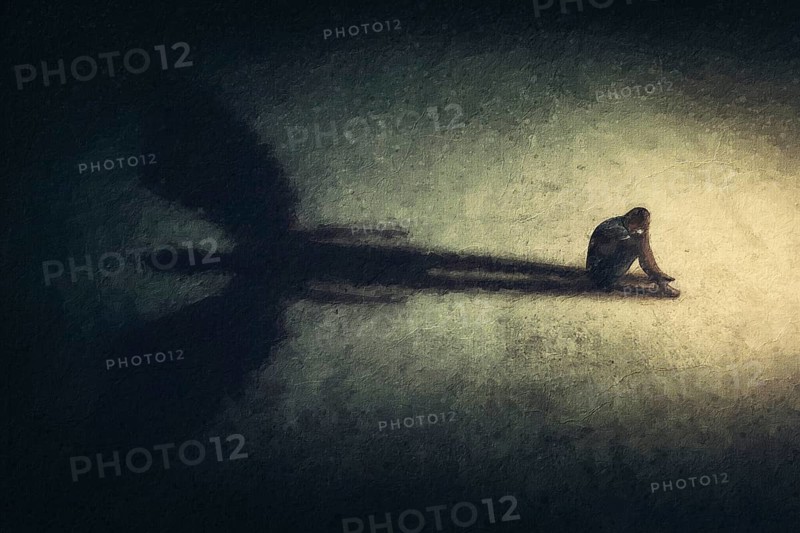 Surreal painting of a man sitting alone isolated in a dark room, casting a shadow of a powerful guardian angel. Inner strength metaphor. Introvert person found an imaginary friend