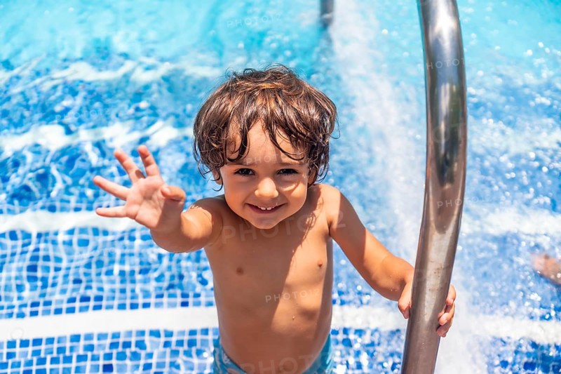 Two year old boy enjoying summer in a swimming pool, smiling on vacation from the water