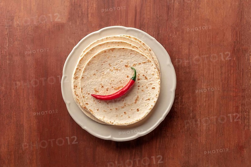 A red chili pepper, shot from above on a pile of tortillas, Mexican flatbreads, on a dark rustic wooden background with copy space