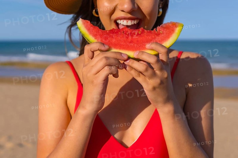 Portrait of a woman eating a watermelon by the beach. Cutout of mouth smiling with red bikini