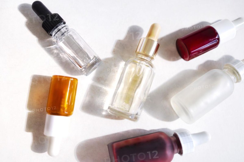 Serum with collagen and peptides in colorful glass bottles on light background with sunlight shadow. Skincare essence for beautiful healthy skin. Top view