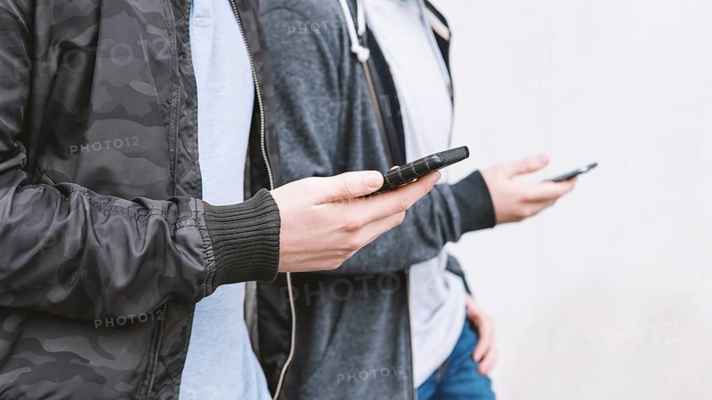 two unrecognizable antisocial mobile phone addicted male teenagers using smartphone, technology concept with copy space
