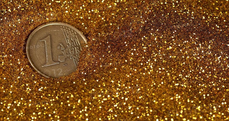 Coin of 1 Euro Rolling on Gold Powder against Black Background