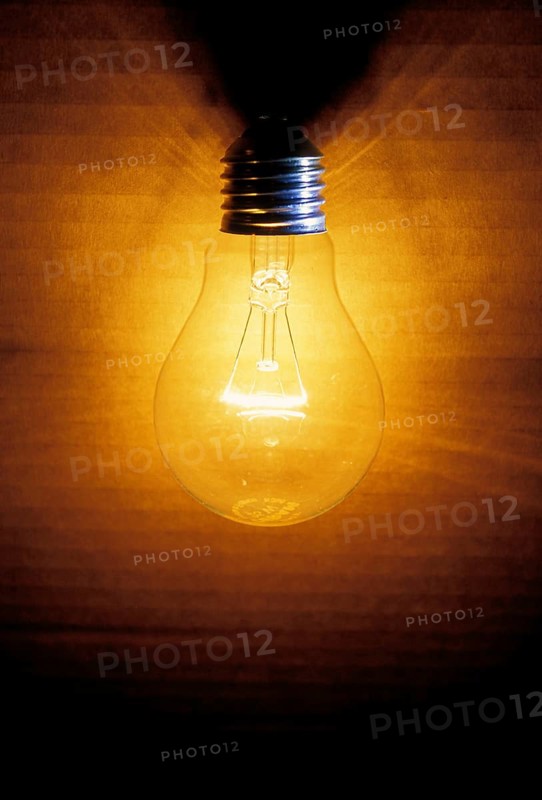 Closeup of an old burning light bulb, switched on, a carton as background is illuminated, lit with a warm yellow and orange light