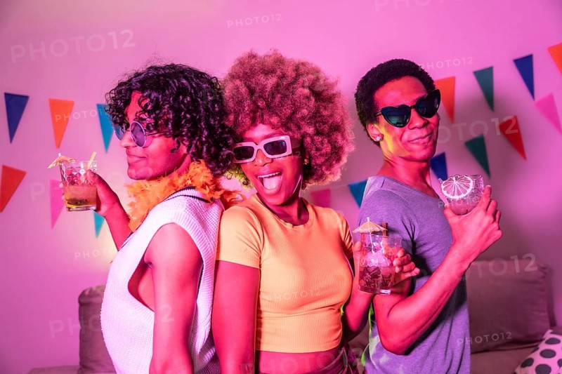 Happy diverse friends laughing partying and drinking alcohol at night with colorful neon light illuminating the apartment