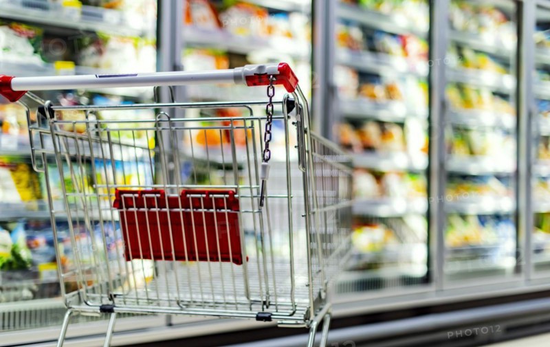 A shopping cart by a store shelf in a supermarket