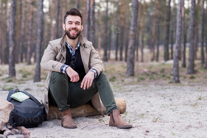 Portrait smiling male traveler sitting beach with his backpack