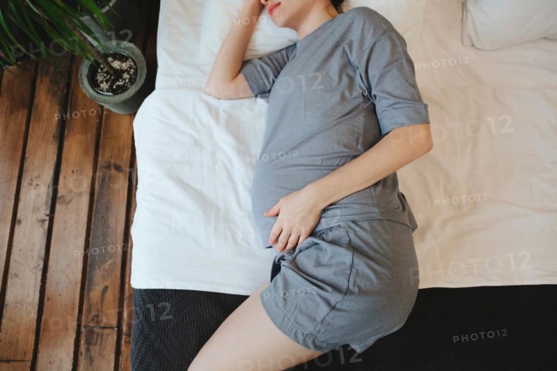 View from above of pregnant woman relaxing resting on couch at home, expectant mother lying on sofa holding belly touching tummy, cropped shot. Pregnancy, maternity and prenatal period concept