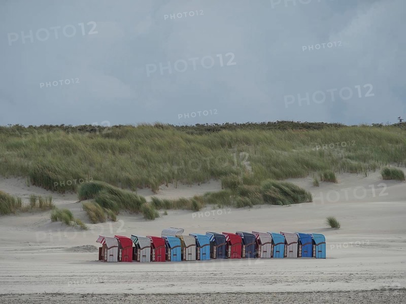 Row of colourful beach chairs along a sandy beach with high dunes in the background under a cloudy sky, Juist, North Sea, Germany, Europe