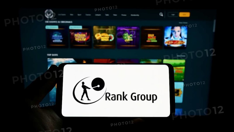 Stuttgart, Germany, 09-15-2022: Person holding smartphone with logo of British gambling company The Rank Group plc on screen in front of website. Focus on phone display, Europe