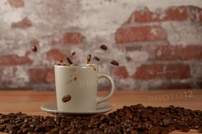Appetizing cup of coffee with coffee beans splashing on a wooden table with a brick background