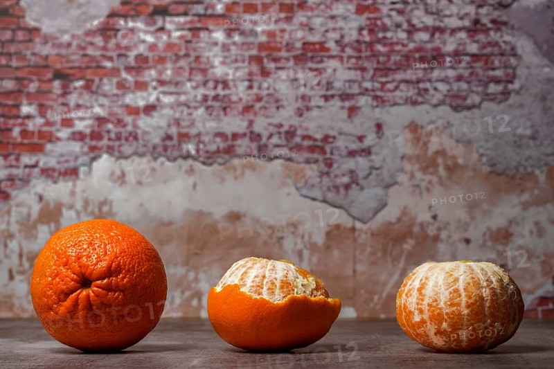 Close-up of whole, peeled tangerines (oranges) (mandarins) (clementines) (citrus fruits) on a table with a brick wall in the background