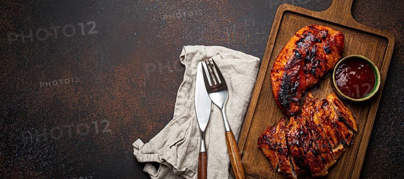 Grilled turkey or chicken marinated fillet with red sauce served and sliced on wooden cutting board on stone brown background from above, poultry breast barbecue space for text