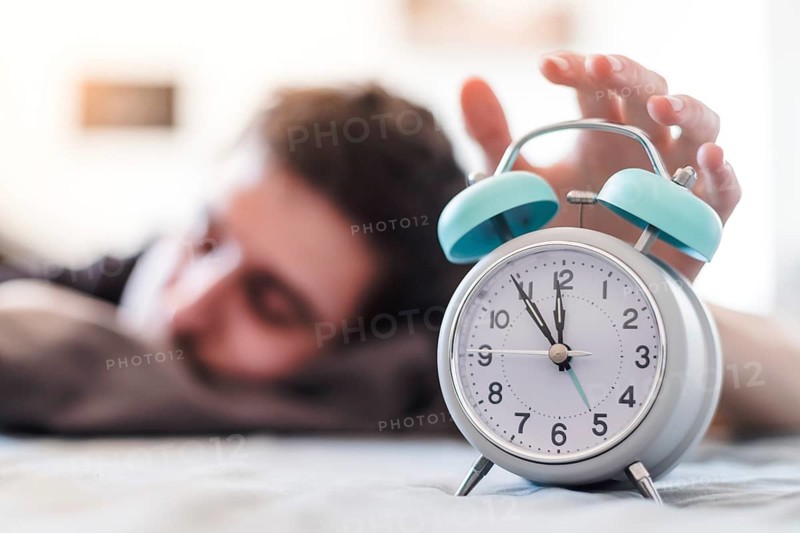 White alarm clock in the morning. Young man wakes up