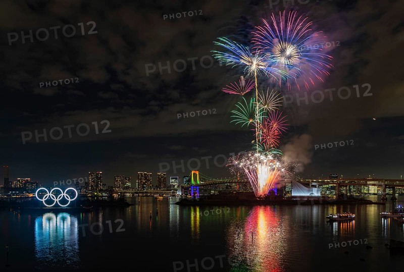 A picture of the fireworks commemorating the opening of the Olympic Rings in the Tokyo Bay, featuring the Rainbow Bridge, at night (Tokyo)