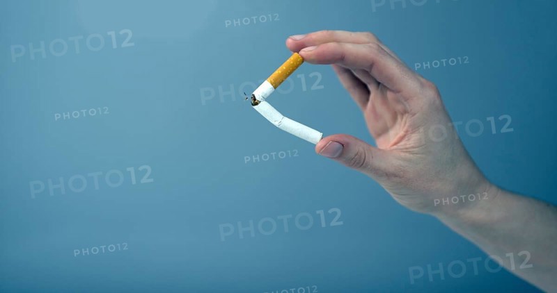 Hand breaking a cigarette against blue background