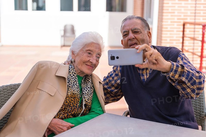 Two very happy elderly people in the garden of a nursing home, looking at the phone