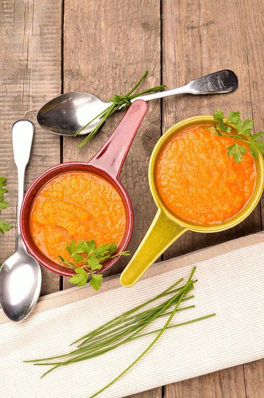 Top view of two rustic bowls with carrot soup on a wooden table