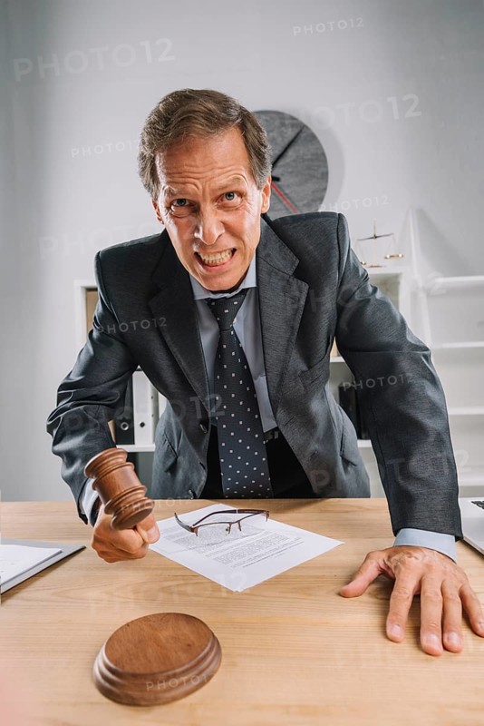 Angry mature judge striking his gavel table courtroom